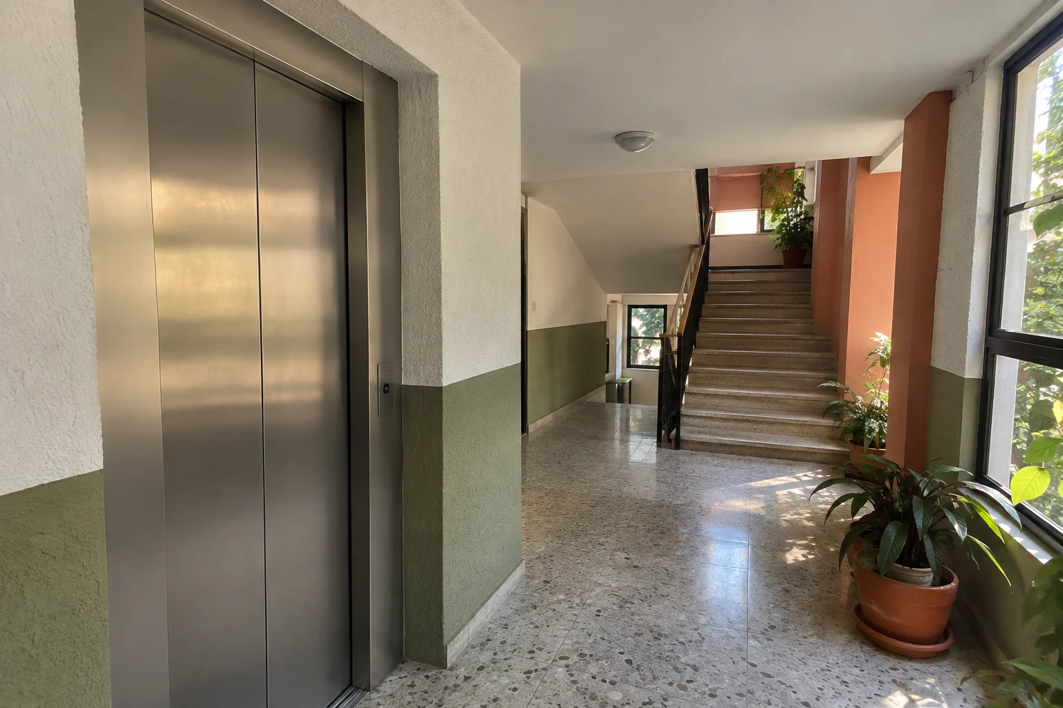 Pasillo común con luz natural, puertas de elevador cerradas y escalera al fondo.
