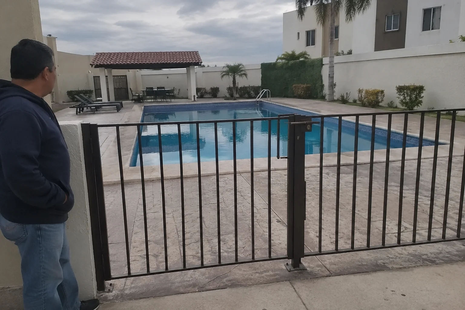 Portón cerrado ante una alberca vacía en una comunidad residencial; escena ilustrativa.