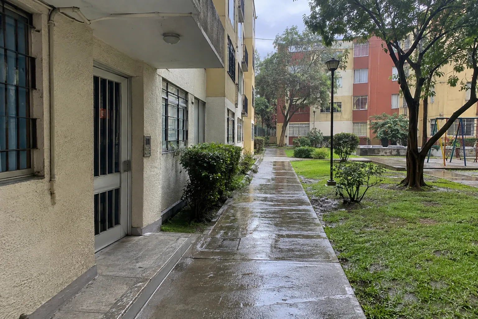 Sendero mojado junto a las entradas de un edificio y un jardín común