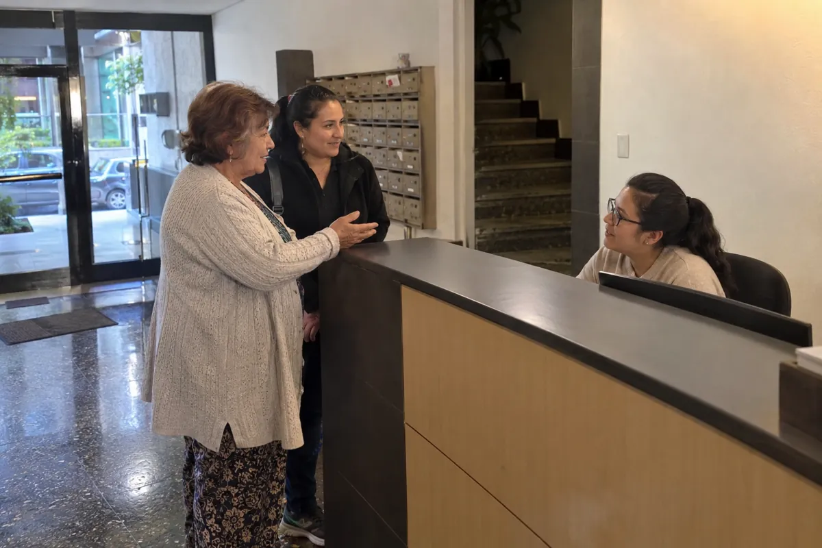 Dos mujeres conversan con otra mujer sentada detrás de un mostrador de recepción