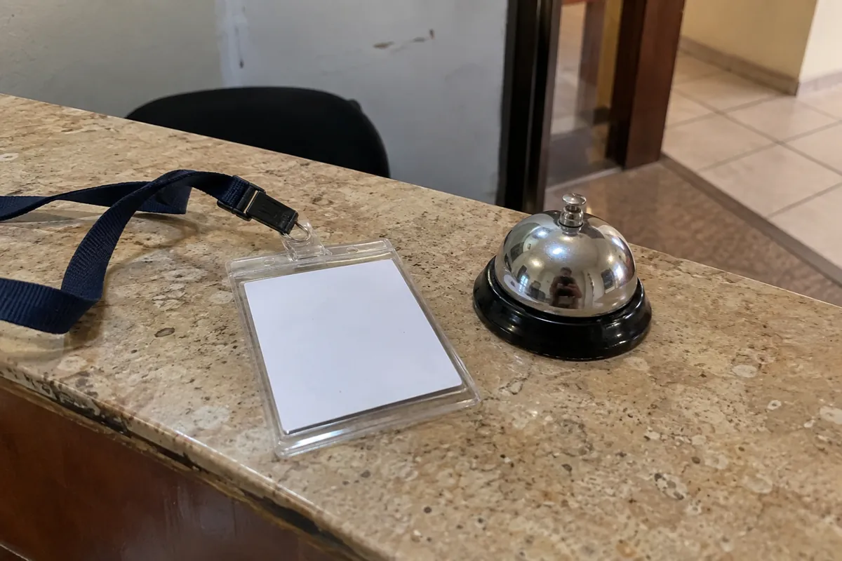 Un portacredencial con tarjeta blanca y una campanilla metálica están sobre un mostrador