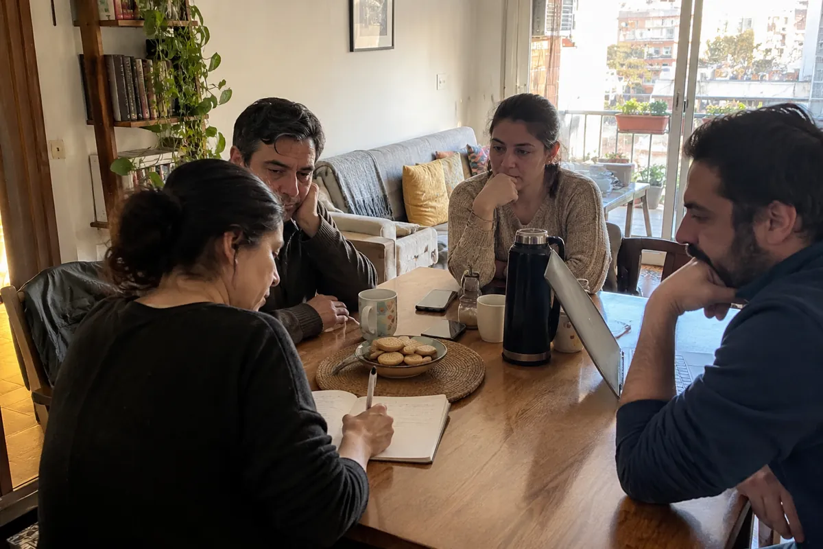 Una mujer toma notas en una libreta mientras otras tres personas conversan alrededor de una mesa
