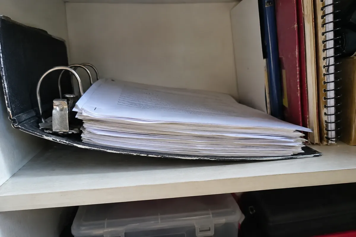 Carpeta de anillas gastada con hojas apiladas en un estante junto a otros documentos