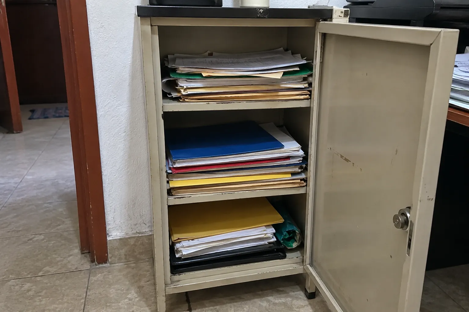 Gabinete metálico abierto con carpetas y documentos apilados en tres repisas