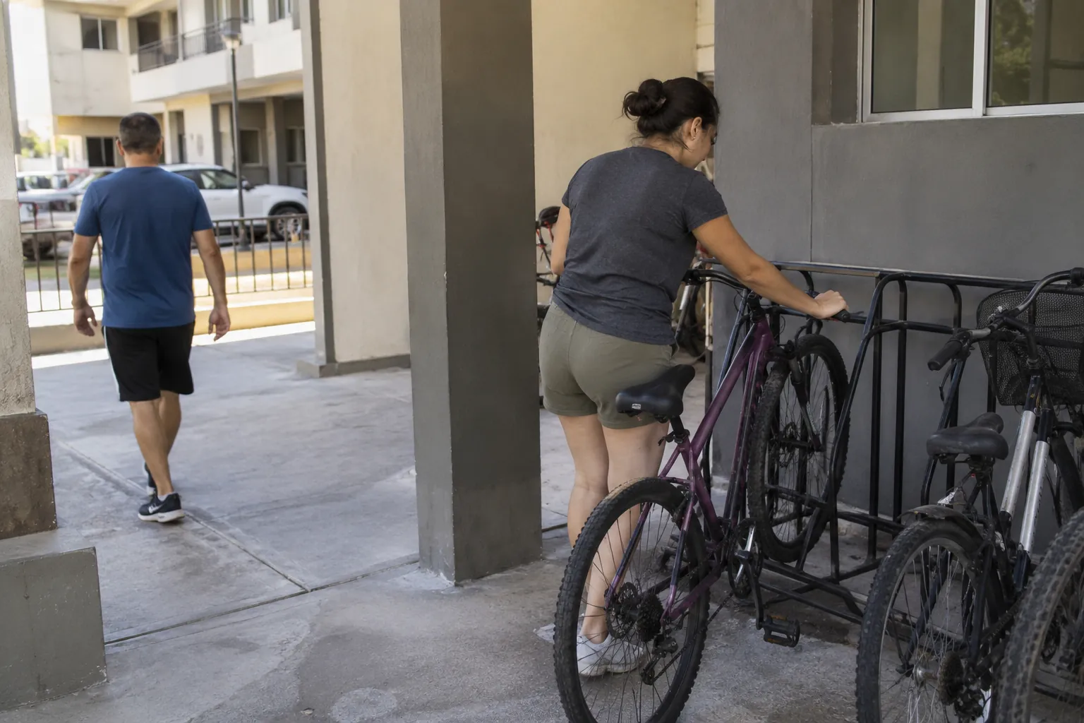 Una mujer acomoda una bicicleta en un soporte mientras un hombre camina por el paso contiguo