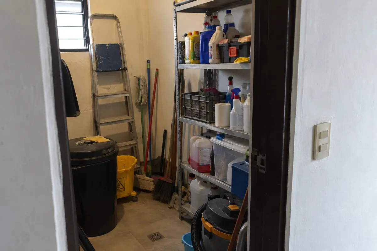 Cuarto de mantenimiento con estantes, productos de limpieza, escobas y una escalera