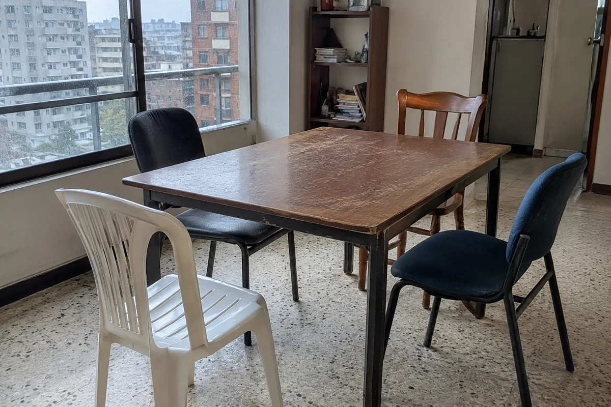 Cuatro sillas diferentes alrededor de una mesa desgastada junto a una ventana