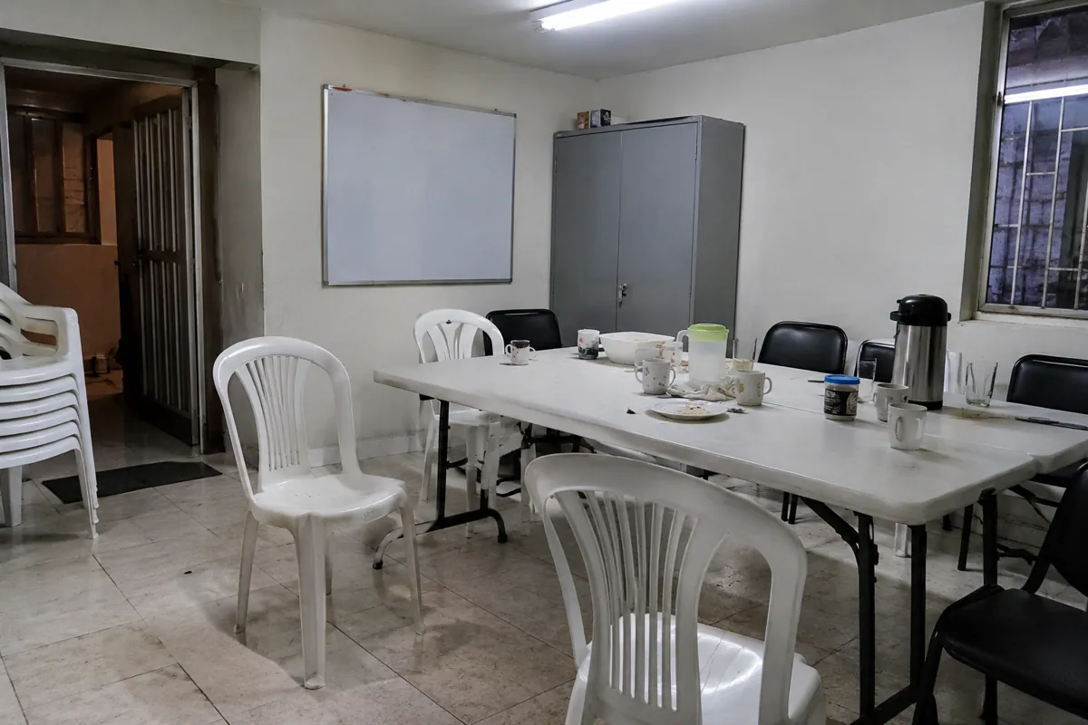 Mesas con tazas y una jarra rodeadas de sillas desacomodadas en un salón vacío