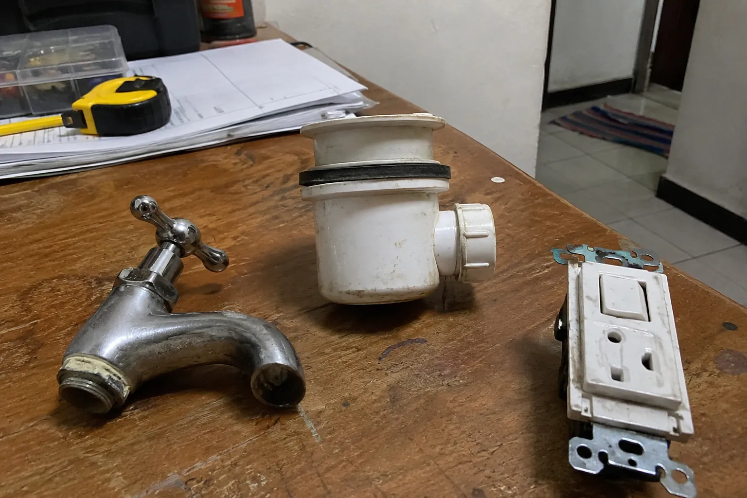 Llave de agua, pieza de desagüe y módulo eléctrico desmontados sobre una mesa
