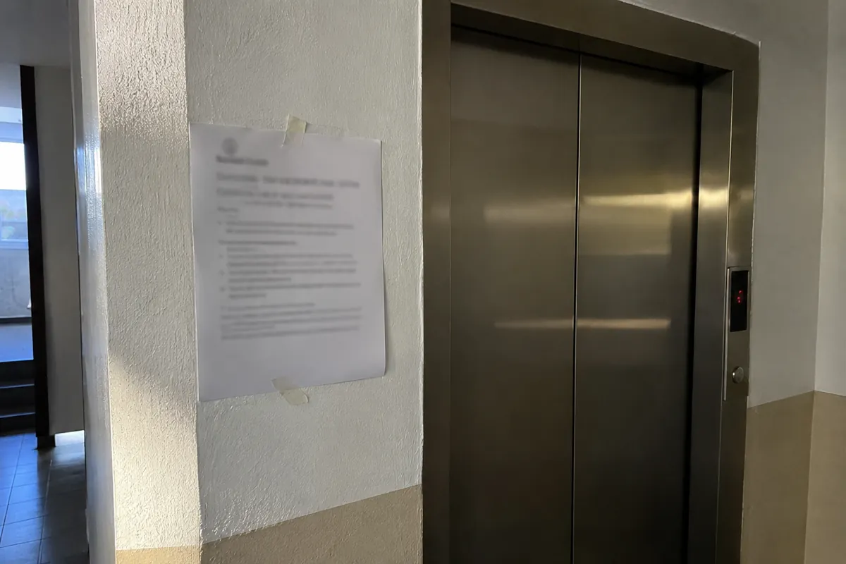 Hoja con texto ilegible fijada con cinta a la pared junto a las puertas de un elevador