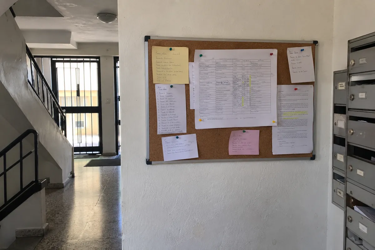 Tablero de avisos con hojas impresas y anotaciones manuscritas junto a los buzones de un edificio
