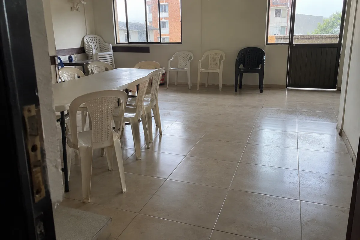 Salón comunitario con una mesa, sillas junto a la pared y un espacio de paso despejado