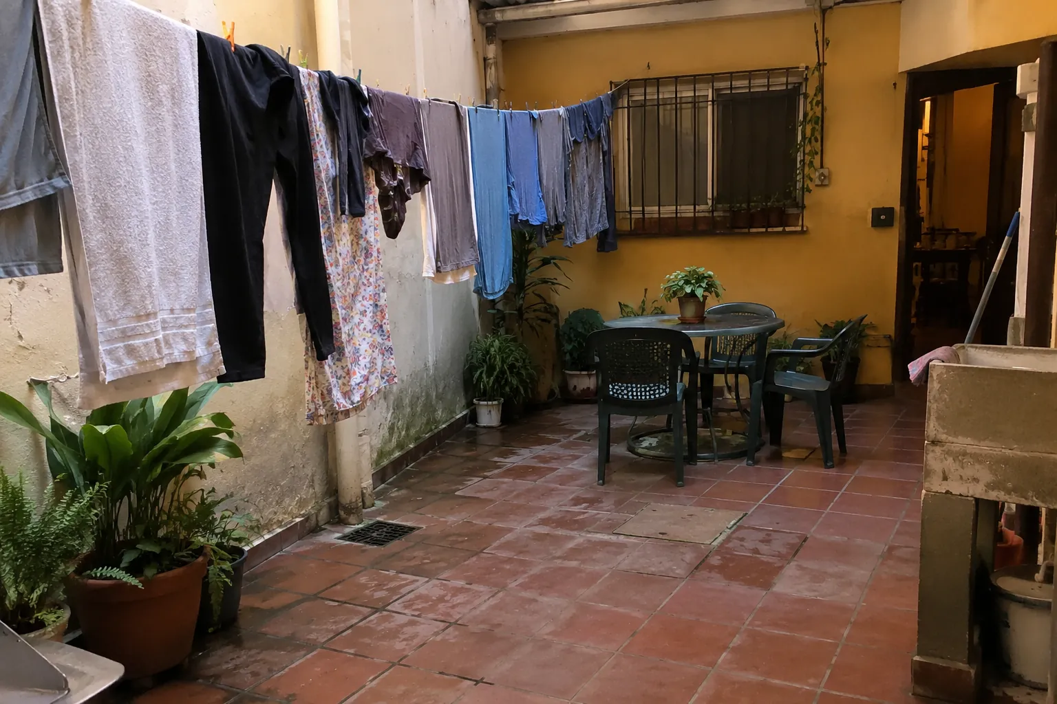 Patio con ropa tendida, plantas y una mesa rodeada de sillas