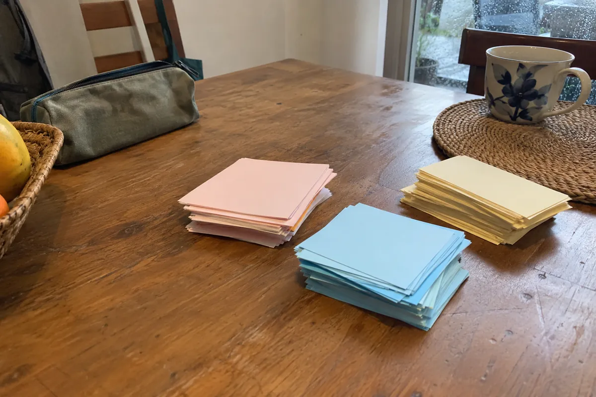 Tres pilas de tarjetas de colores sobre una mesa junto a una ventana con gotas de lluvia