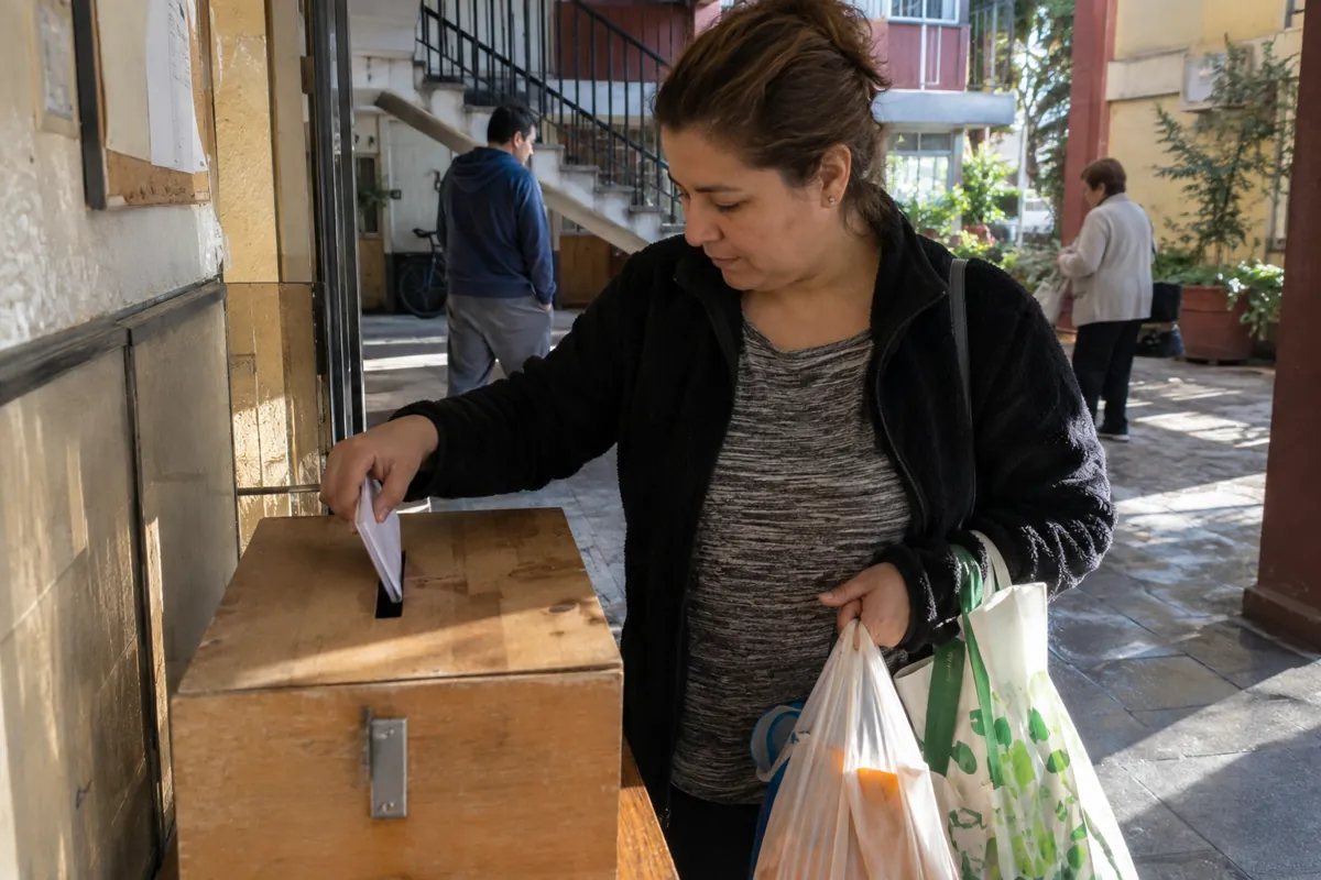 Una mujer con bolsas de compras introduce un papel doblado en una caja con ranura