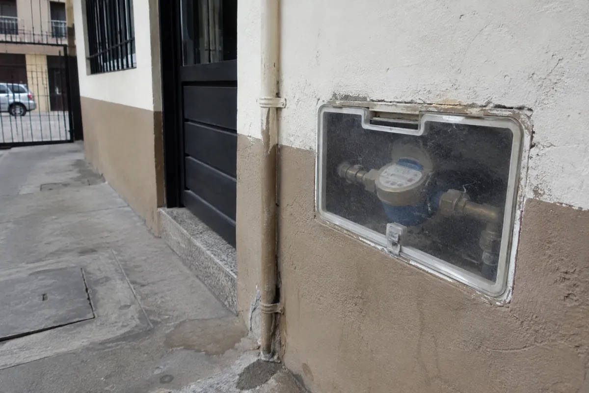 Medidor de agua dentro de una caja con cubierta transparente cerrada, junto a una puerta