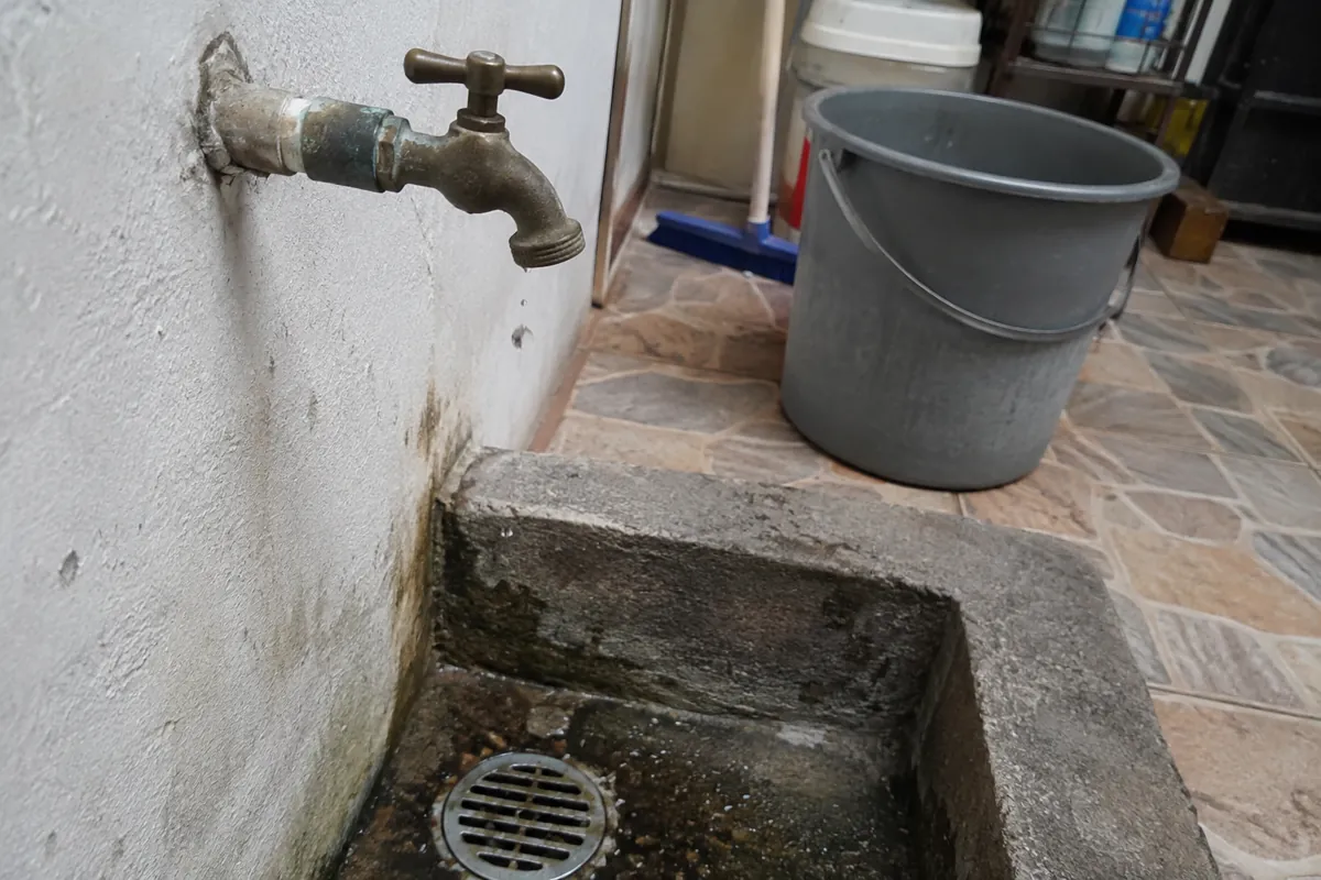 Llave de agua con gotas sobre un desagüe junto a una cubeta