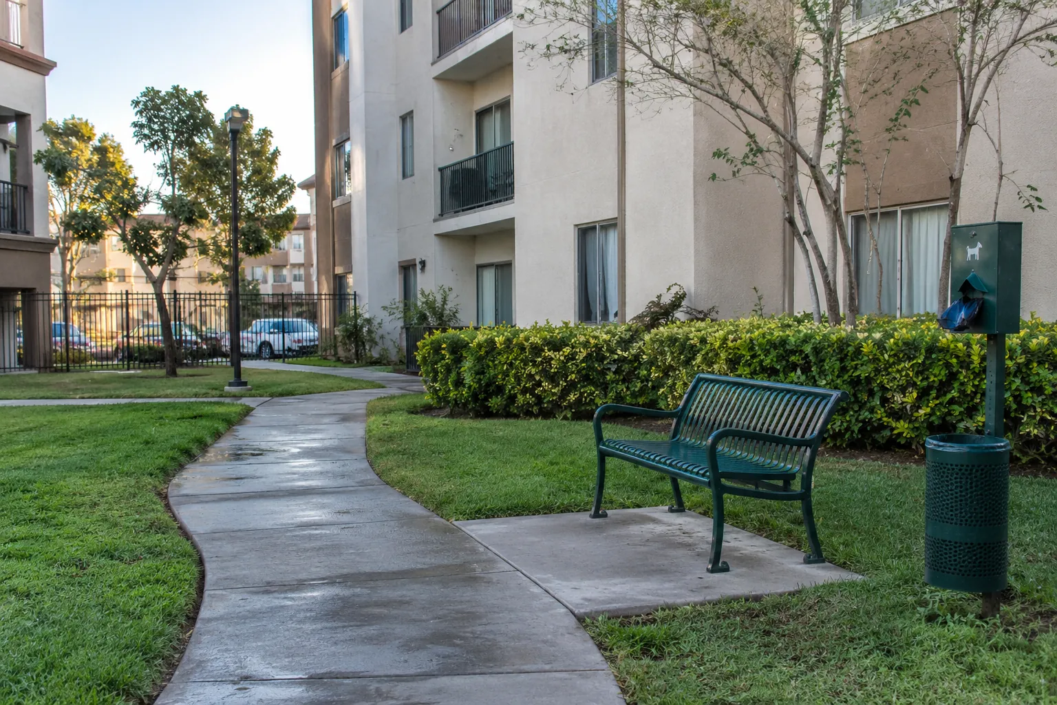Sendero de un patio residencial junto a una banca y un dispensador de bolsas para mascotas