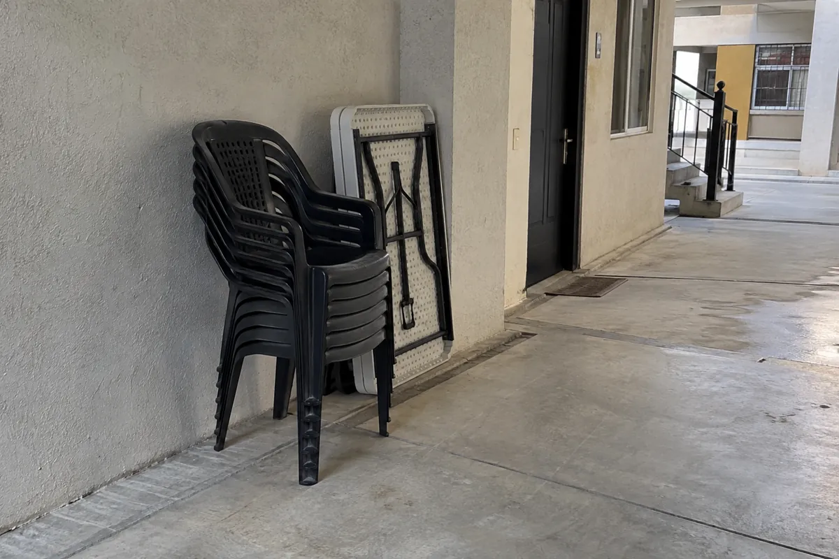 Sillas apiladas y una mesa plegada junto a la pared sin ocupar el paso del corredor