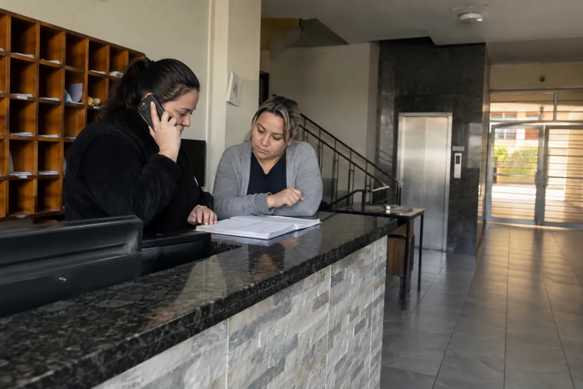 Dos mujeres revisan una libreta en recepción mientras una habla por teléfono