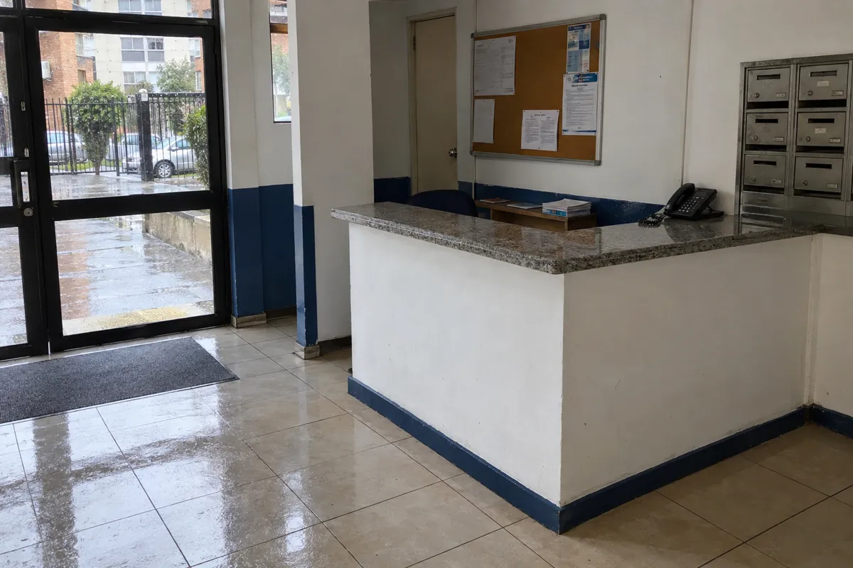 Mostrador de recepción con teléfono, buzones y tablero de avisos junto a la entrada