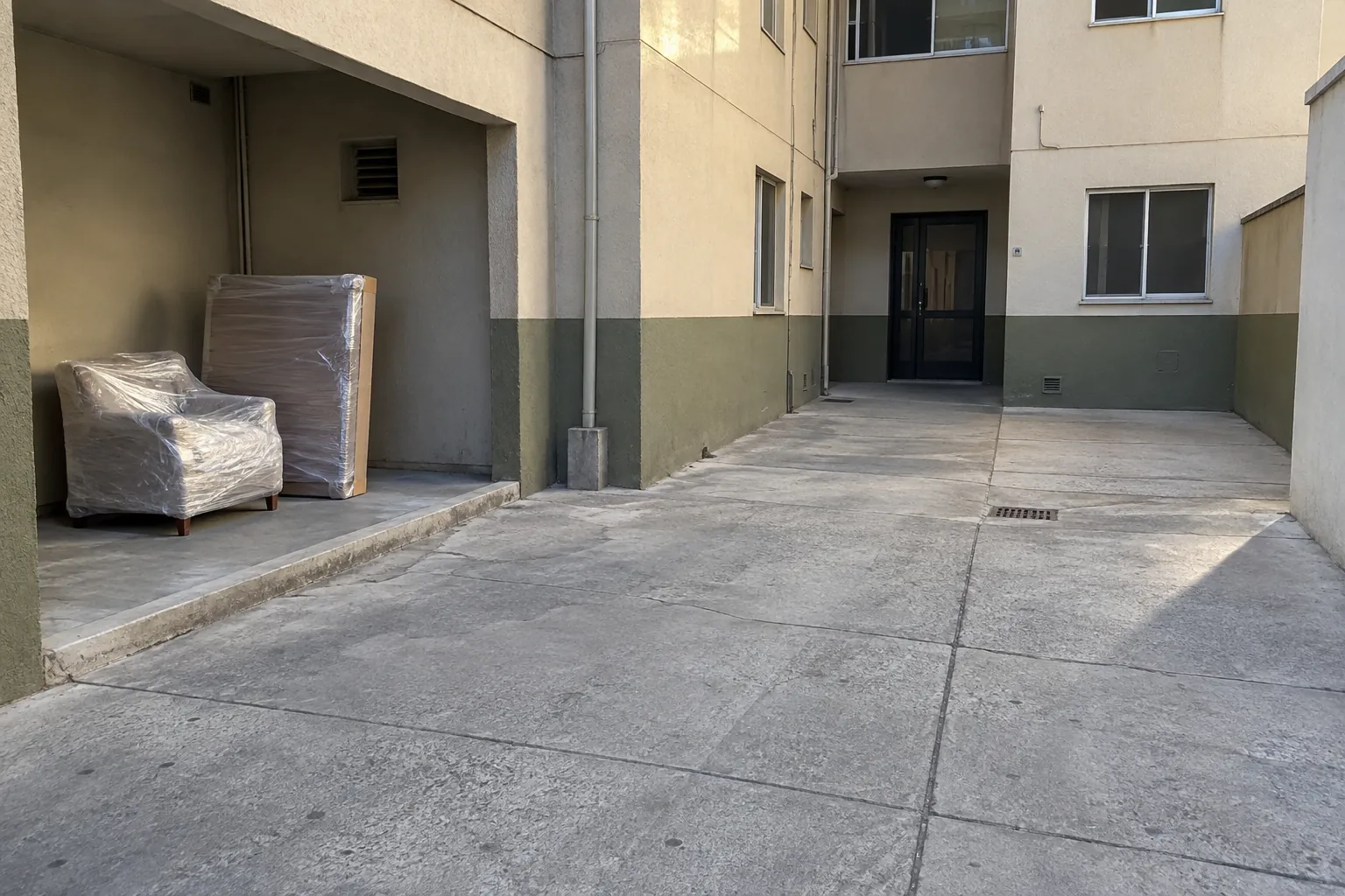 Sillón y panel protegidos con envoltura en un espacio lateral de un patio, separados de la entrada despejada