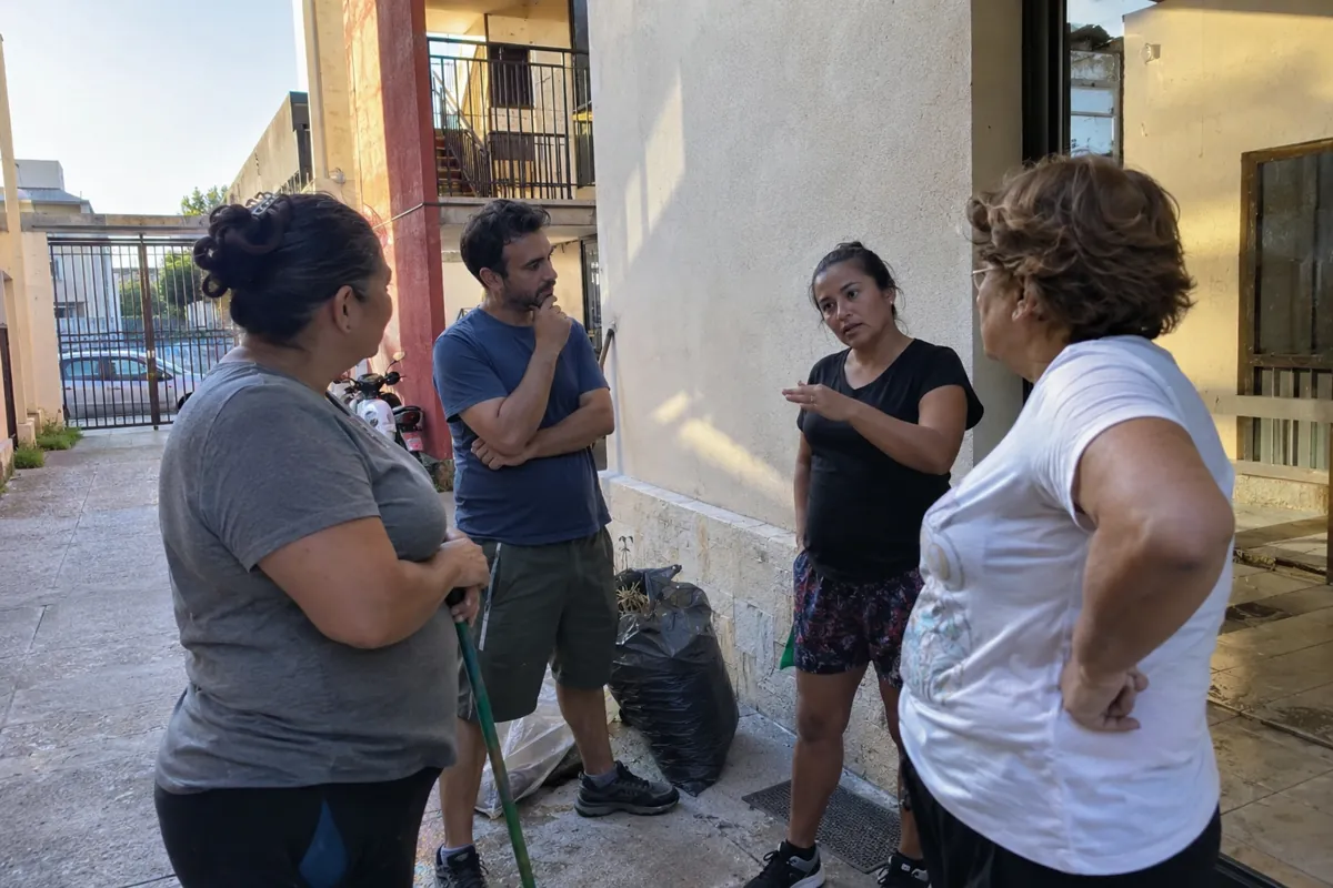 Cuatro personas adultas conversan de pie en un patio junto a utensilios de limpieza
