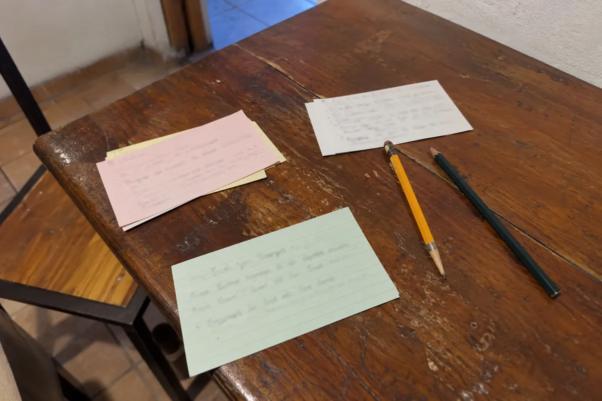 Tarjetas de papel con escritura desenfocada y dos lápices están sobre una mesa rayada