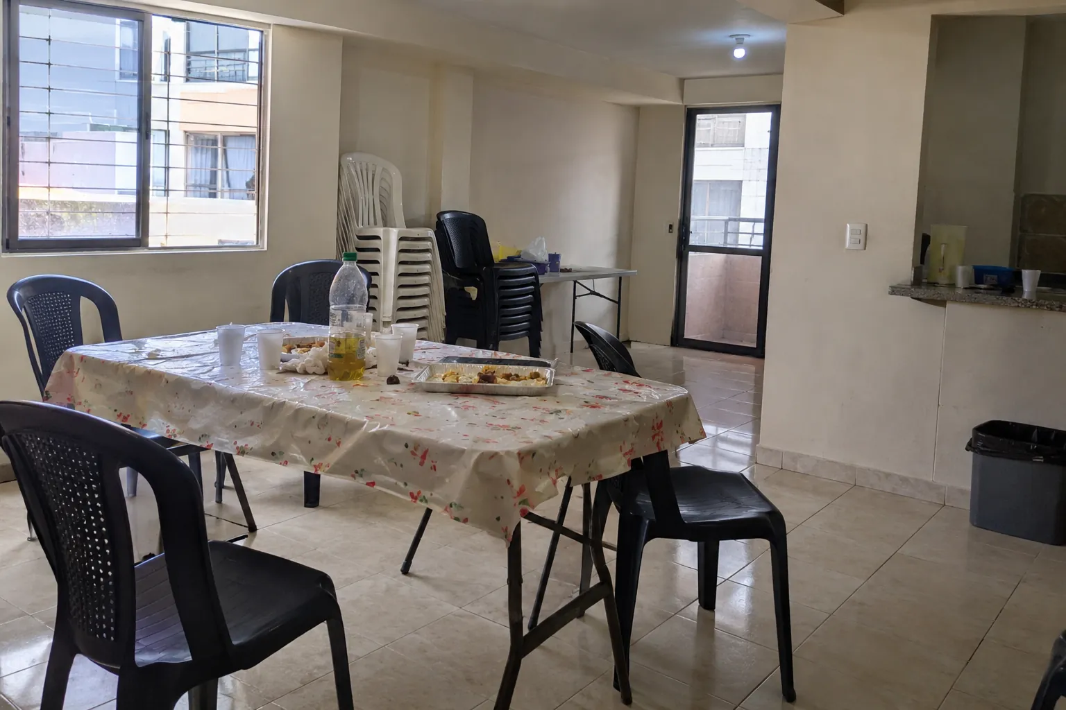 Mesa con vasos y restos de comida en un salón con sillas sueltas y otras apiladas al fondo