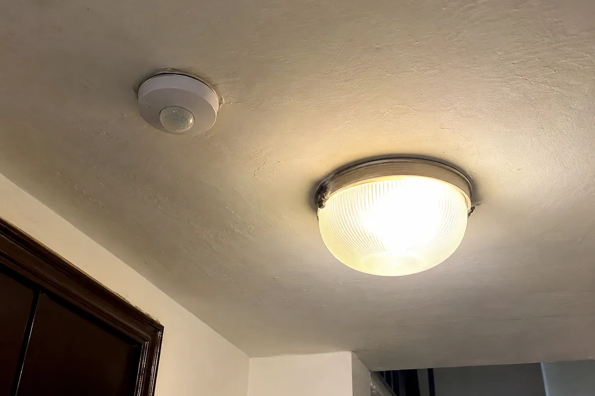 Lámpara encendida y sensor redondo instalados en el techo de un pasillo