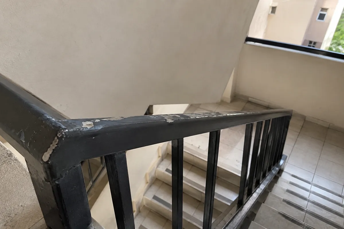 Pintura desgastada en un barandal metálico junto a una escalera interior