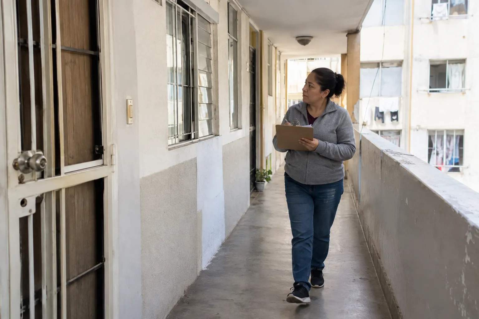 Mujer con portapapeles recorriendo un pasillo de departamentos