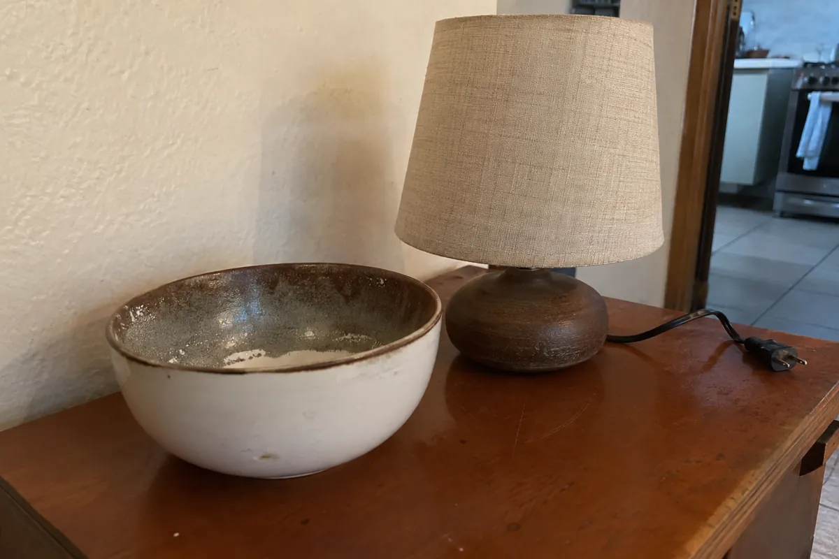 Un recipiente de cerámica y una lámpara desenchufada descansan sobre un mueble