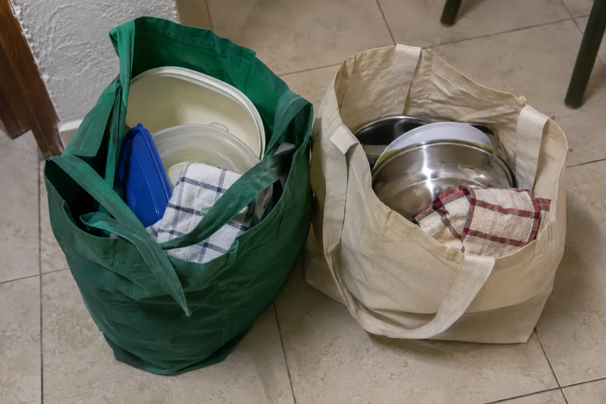 Dos bolsas reutilizables con recipientes de cocina y paños sobre el piso