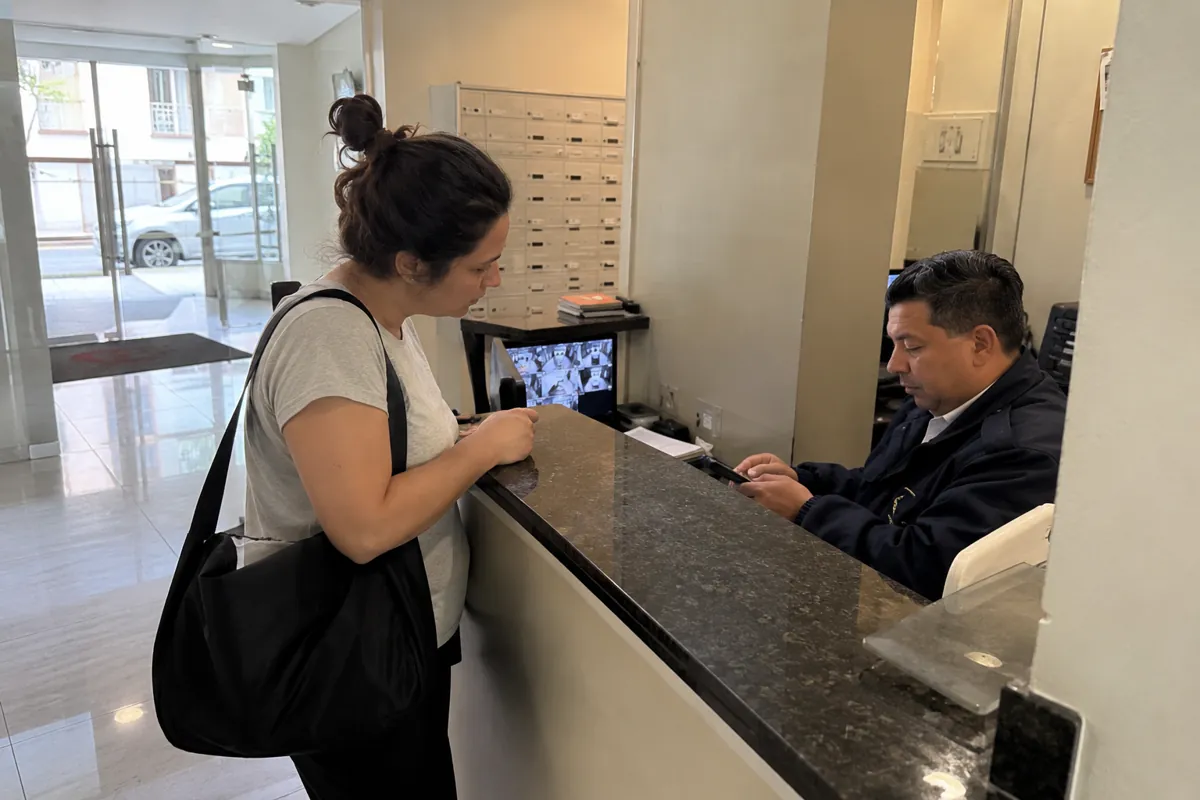 Mujer junto a un mostrador mientras un hombre sentado detrás consulta un teléfono