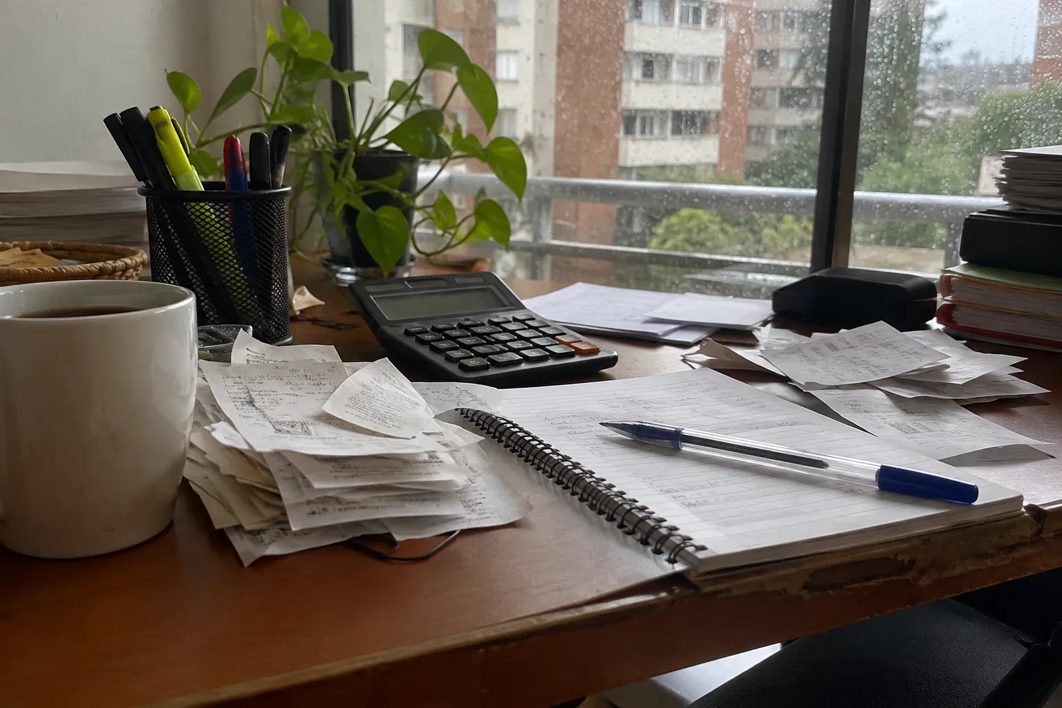 Recibos, calculadora y libreta abierta sobre un escritorio junto a una ventana