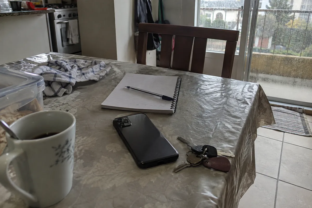 Teléfono boca abajo, libreta abierta y llaves sobre una mesa junto a una ventana