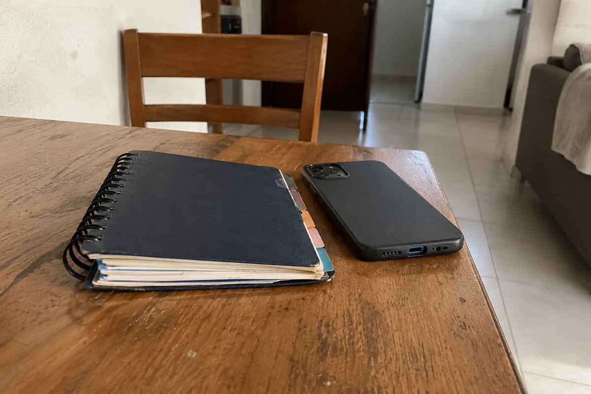 Un teléfono colocado boca abajo y una libreta de contactos cerrada descansan sobre una mesa