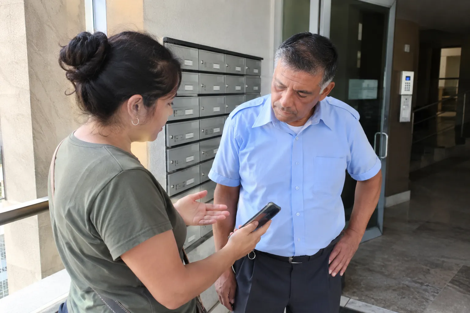 Una mujer sostiene un celular mientras conversa con un hombre junto a los buzones de un edificio