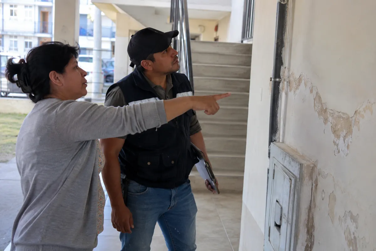 Dos personas observan una pared con pintura desprendida junto a una tubería