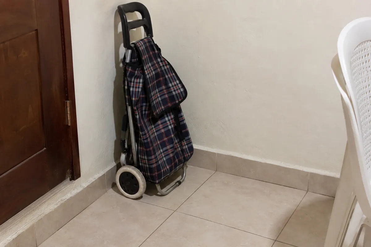 Carrito de compras plegado con bolsa de cuadros guardado junto a una pared