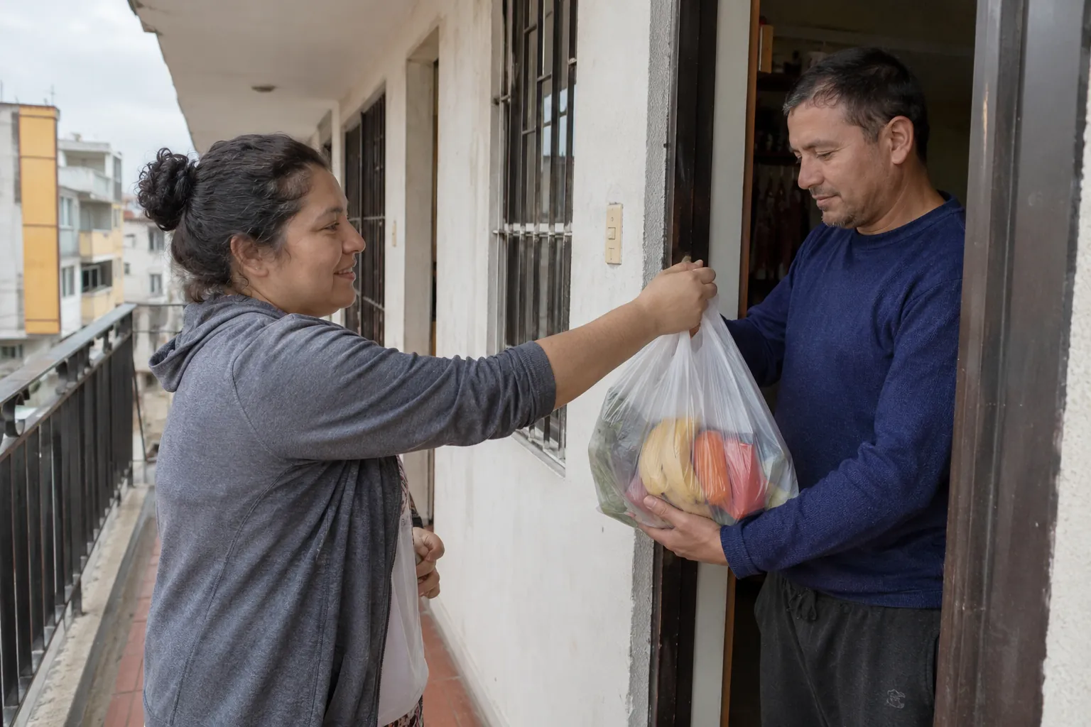 Una mujer entrega una bolsa de alimentos a un hombre en la puerta de una vivienda