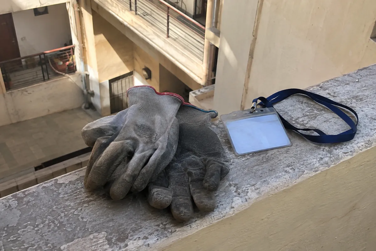 Guantes de trabajo usados y un portacredencial con cinta descansan sobre un borde de concreto