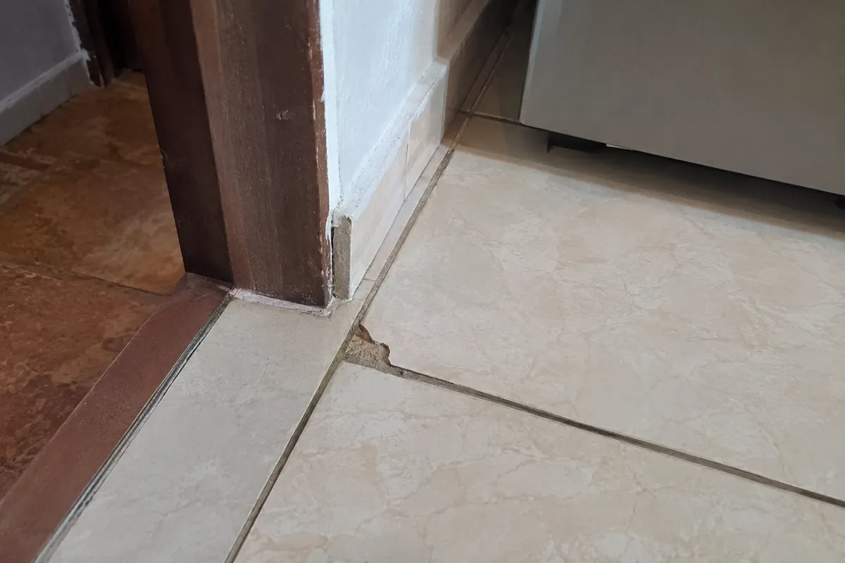Esquina despostillada de una baldosa junto al marco de una puerta