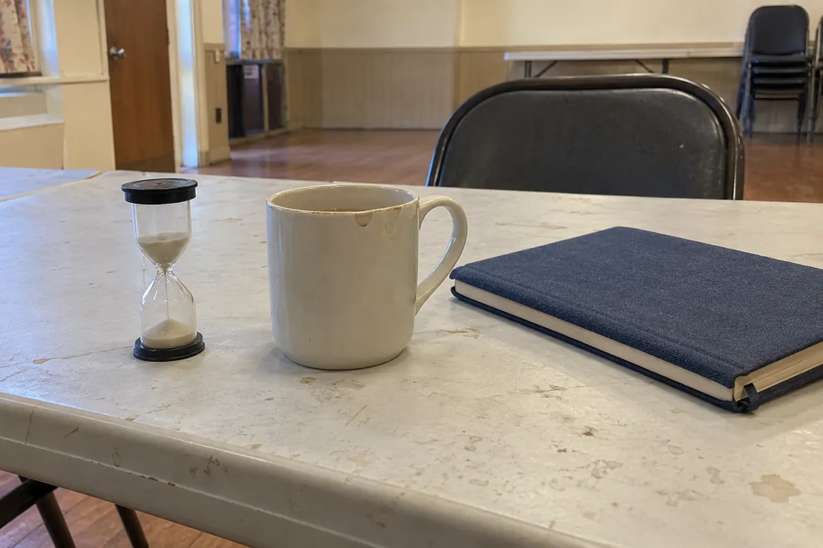 Reloj de arena, taza y libreta cerrada sobre una mesa de un salón comunitario