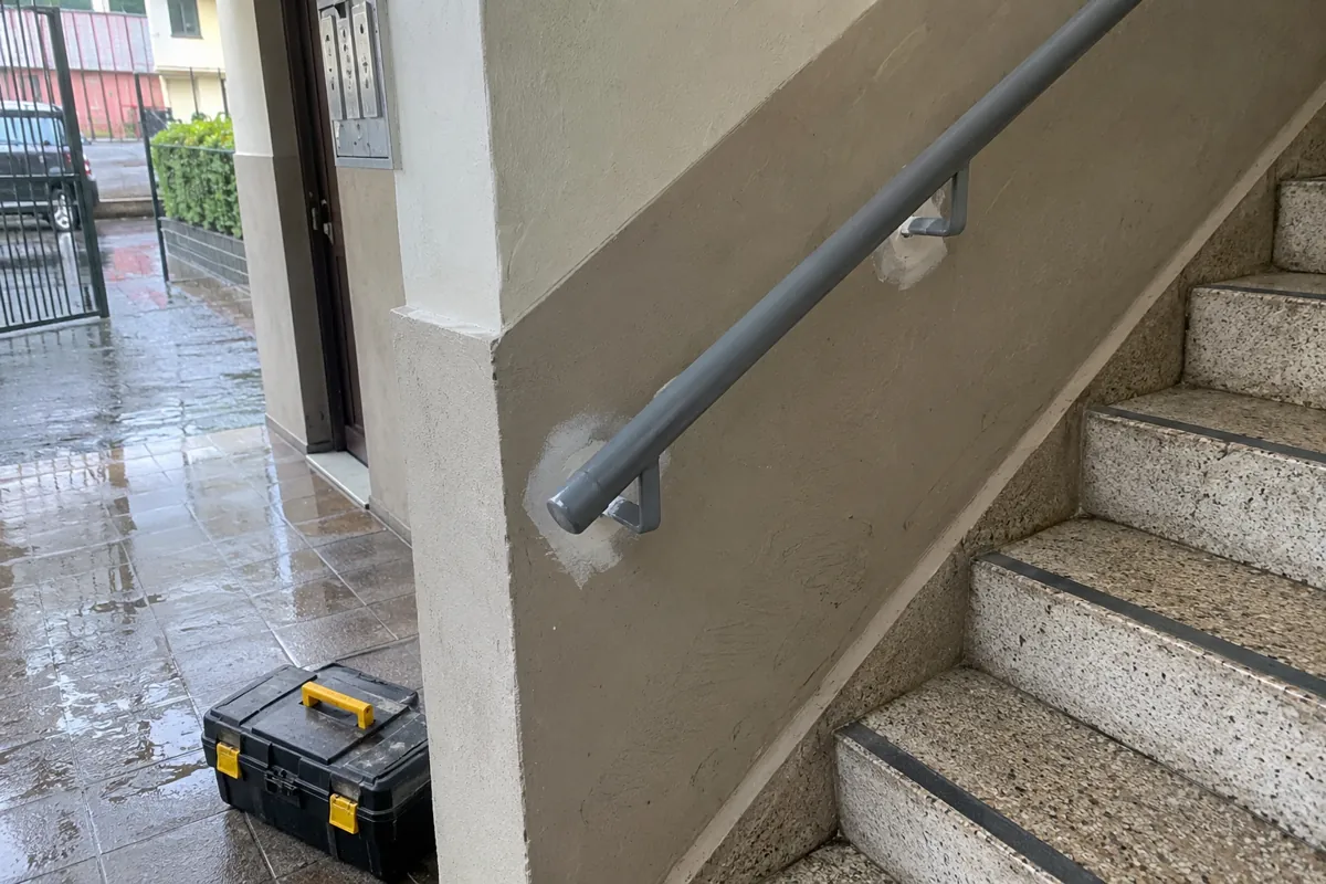 Caja de herramientas cerrada junto a una escalera y un pasamanos con resanes en la pared