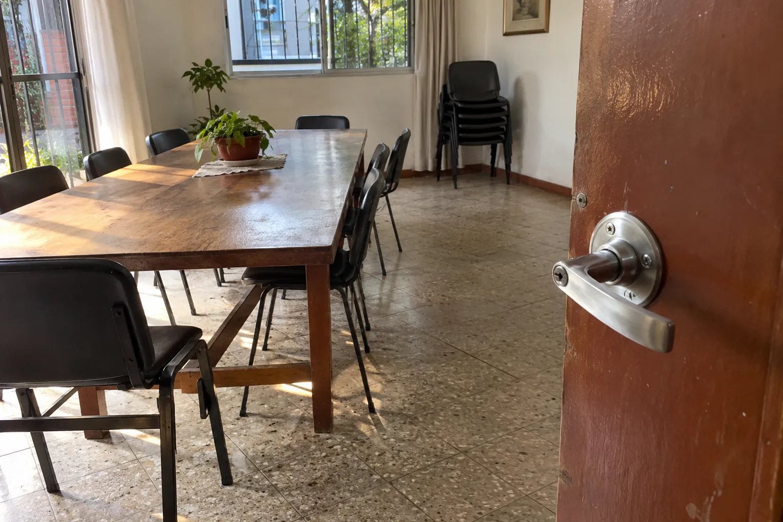 Puerta abierta con manija metálica y un salón con mesa y sillas al fondo