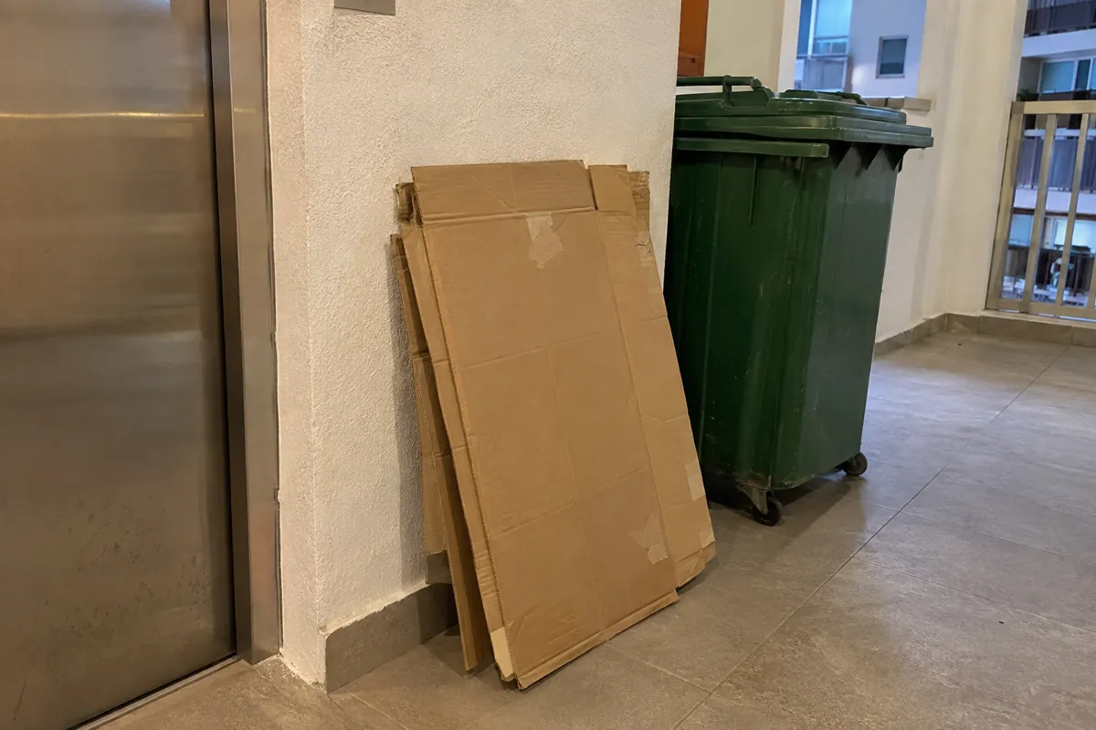 Cajas de cartón aplanadas apoyadas junto a un contenedor con ruedas