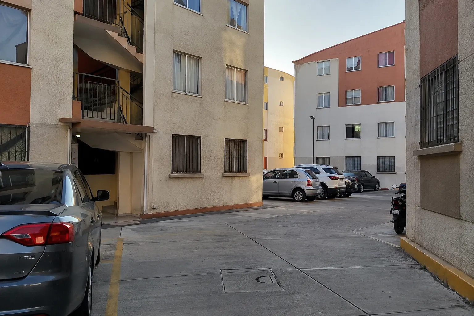 Patio pavimentado entre edificios residenciales con autos estacionados a los lados