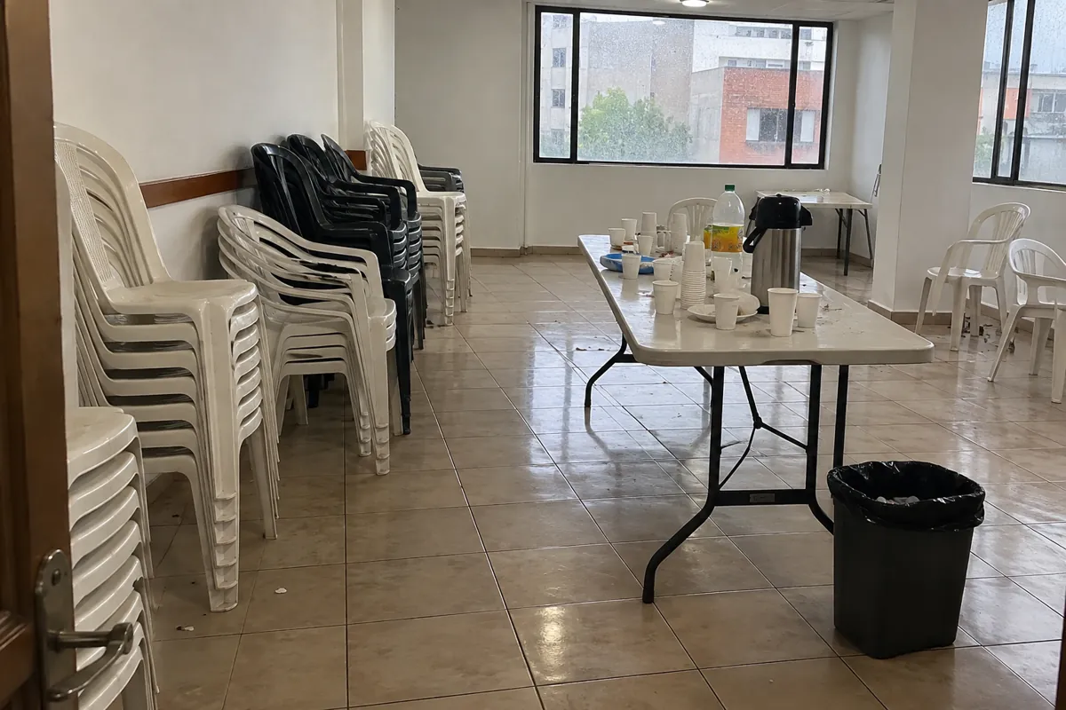 Sillas apiladas y vasos reunidos sobre una mesa en un salón comunitario vacío